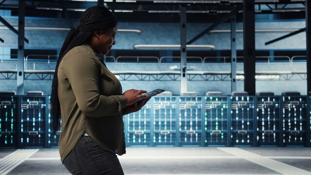 Smiling data center technician using tablet to manage software updates for system stability. Upbeat IT expert in server room configuring infrastructure with device for optimum performance, camera A