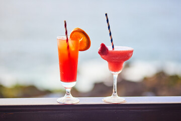 Fototapeta premium Two colorful tropical cocktails served on a balcony railing with a blurred ocean view in Tenerife, Canary Islands, Spain.