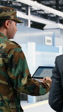 Vertical video Microelectronics factory technician and soldier analyze EDA software schematics to increase microchips production. Government looking to upgrade national semiconductors manufacturing