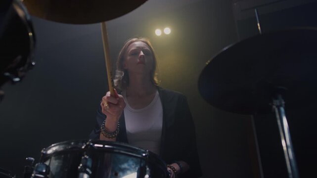 Woman drummer plays a drum kit, drumstick. Female musician beats a rock rhythm on drums, cymbals. Girl artist is rehearsing in a room or performing on festival stage. Alternative indie band in club