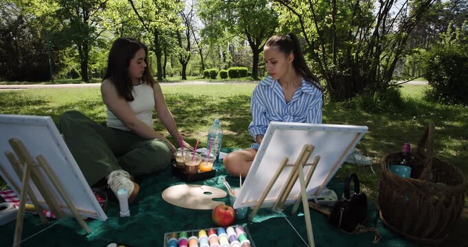 Two Young Women Paint and Relax in a Scenic Park, Enjoying Friendship and Nature's Beauty