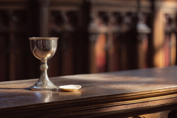 Fototapeta premium Close-up of polished wooden altar with single chalice and wafer, soft natural morning light, calm empty sacred scene.