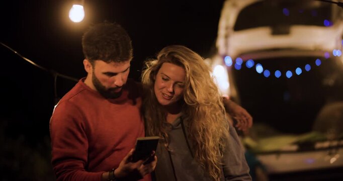Watching a video together under string lights at night while parked at a scenic spot with friends during a weekend trip