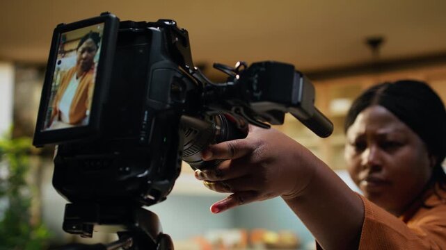 African American woman, close up, setting the tripod and camera, filming preparations in kitchen, influencer adjusting tripod height and camera settings. Balancing light for steady vlog.