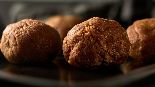 round balls of dark brown jaggery on dark surface, unrefined cane sugar in soft focus, natural sweeteners and south asian ingredients concept