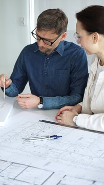 Architects and engineers collaborate over detailed blueprints and a house model, using compass and drafting tools to plan modern residential development with focused teamwork
