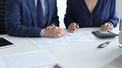 Obraz premium Business colleagues are reviewing financial reports and using a calculator during a productive meeting in a brightly lit office setting. Audit and taxes in business