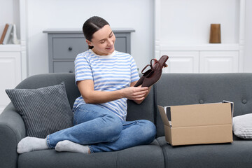 Obraz premium Happy woman taking heeled shoes from open parcel on sofa at home