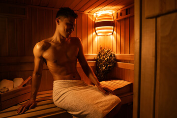 Fototapeta premium Muscular man with drops of sweat sitting on bench in dark sauna