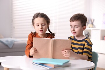 Fototapeta premium Cute little kids reading book at white table indoors