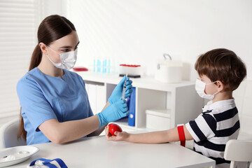Fototapeta premium Nurse drawing little boy's blood sample in clinic
