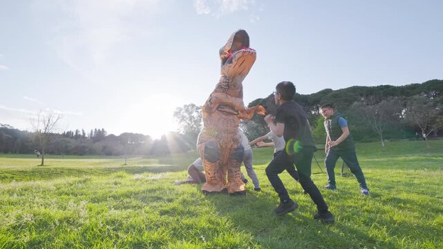 Children chasing and tackling inflatable t-rex costume in park