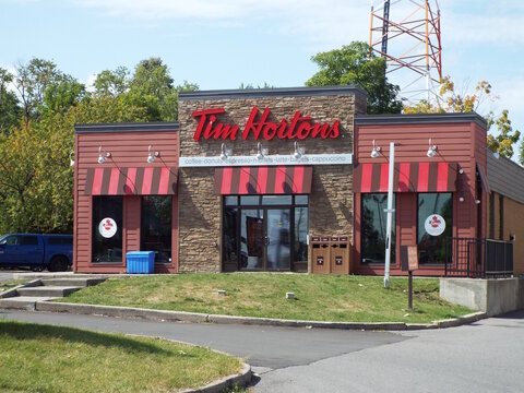 Ottawa, Ontario, Canada-July 23, 2025: A "Tim Hortons" coffee shop storefront is visible behind a metal construction fence and orange traffic barrels on a cloudy day at 993 Richmond Road.