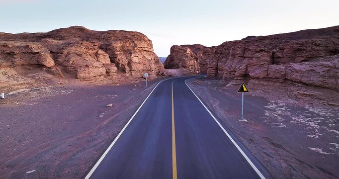 Aerial view of winding asphalt road through rock canyon at dusk, Xinjiang, China. 