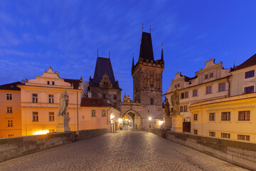 Obraz premium Old Town Bridge Tower on Charles Bridge in Prague, Czech Republic, at dawn with illuminated facades and empty cobblestone roadway.
