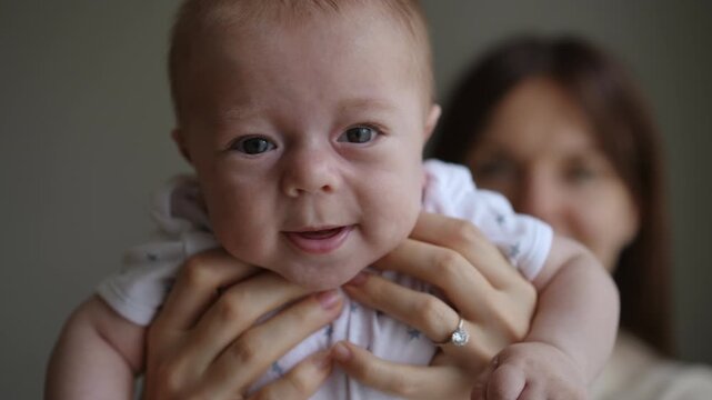 Loving mother holding her infant son. The newborn baby boy is making a lot of funny and cute faces, from crying to smiling and laughing