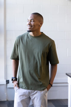 African-American man standing and looking left by cinderblock wall in olive tee with watch