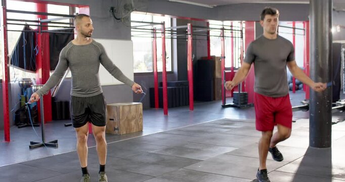 Diverse male friends swinging jump ropes, alternating double and single leg hops at gym