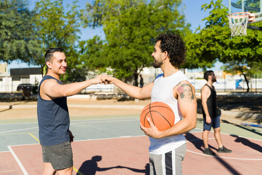 Two male friends on a sunny outdoor basketball court exchanging a fist bump, showing trust and camaraderie