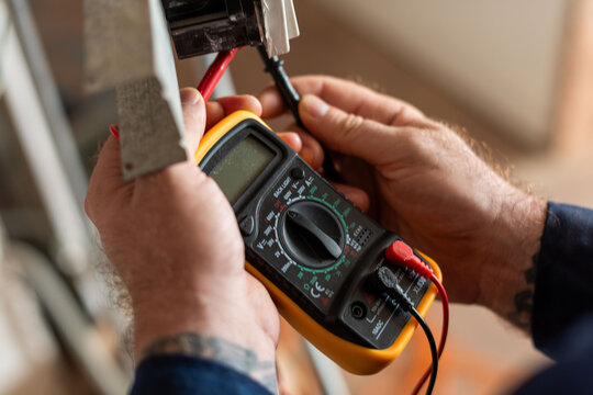 Electrician using digital multimeter tool.