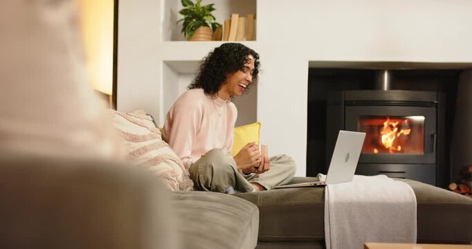 Non-binary adult settling on sofa opening laptop holding coffee mug typing gesturing on call