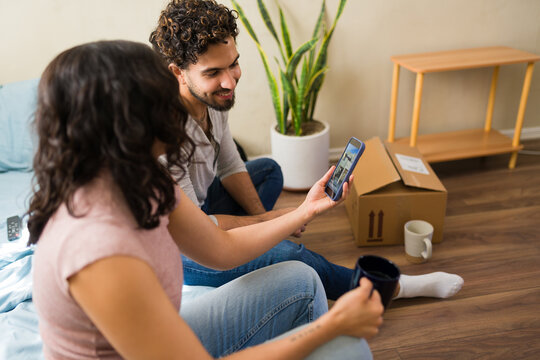 Couple living a humble life, scrolling on smartphone dreaming of a new house while living in their modest apartment
