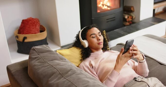 non-binary person picking up smartphone and scrolling content on grey sofa near glowing stove