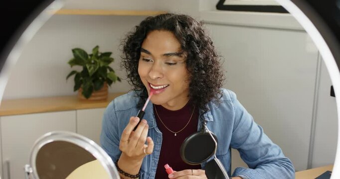 Grabbing gloss at desk, non-binary creator applying pink, inspecting mirror before filming tutorial