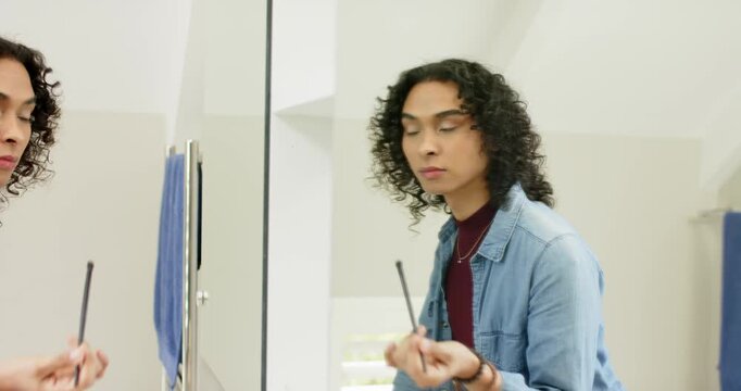 Non-binary person grabbing eyeliner and applying it to define lash line at sink mirror, copy space