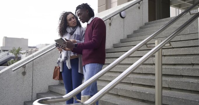 Opening with diverse colleagues stepping onto outdoor steps comparing mobile devices reviewing info