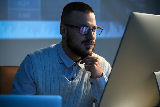 Thoughtful male trader with eyeglasses working in dark office
