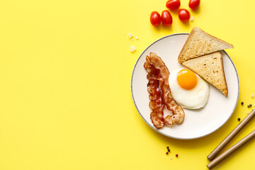 Fototapeta premium Plate with tasty fried egg, bacon and toasts on yellow background