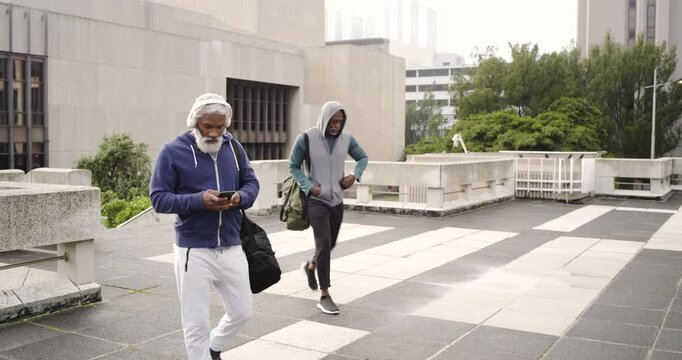 Senior African American male friends entering rooftop wearing headphones while walking together