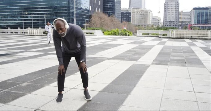 Senior African American man jogging in plaza slowing to walk checking watch monitoring pace