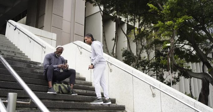 Diverse acquaintances in gym wear sharing water bottle as jogging man requesting hydration on steps