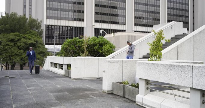 Man descending steps crossing plaza, Black exec with phone starting rolling suitcase toward camera