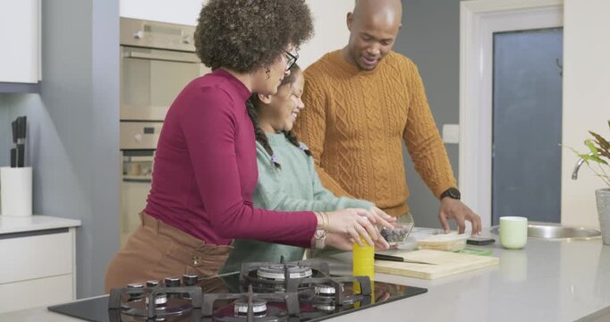 Parents guiding daughter and adding sliced bread and berries into box for school at kitchen island