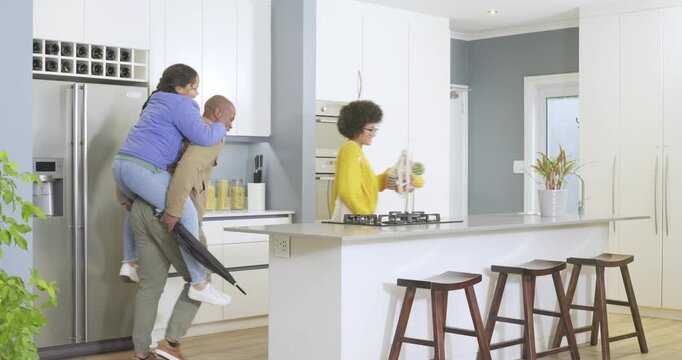 African American family entering kitchen, unpacking apples, teasing each other and sharing laughter