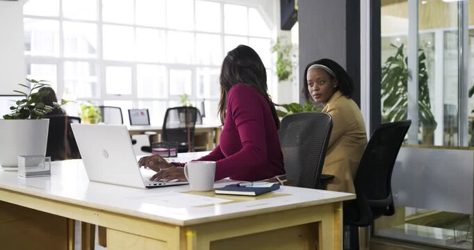 Diverse coworkers after noticing need for review, leaning over laptop at office discussing report