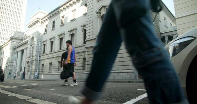 Commuters following pedestrian entering right, walking past stone building to offices carrying bags