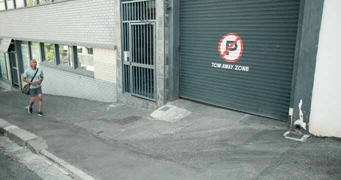 Diverse pedestrians walking after left entry on sloped sidewalk past no parking garage