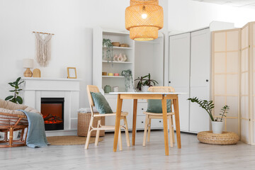Fototapeta premium Interior of stylish dining room with table, armchair, fireplace and glowing lamp