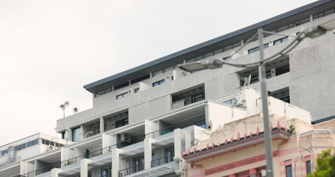 Camera is tilting and panning upward and right, revealing apartment terraces, planters, clock tower