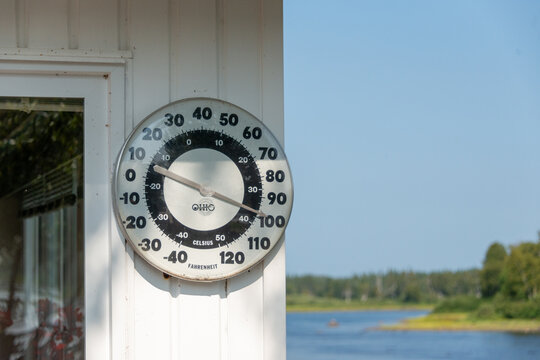 Newfoundland, Canada-April 7, 2026: A round white metal antique jumbo Ohio Thermometer Company thermometer that measures Celsius and Fahrenheit temperatures on an exterior white wall of shed. 