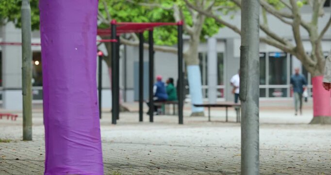 Diverse people in plaza heading to doors, passing purple-wrapped tree after passer blocking camera