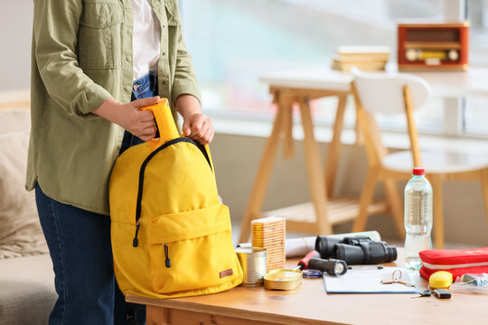 Woman packing emergency backpack with necessities at home
