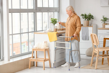 Fototapeta premium Mature woman with walker and cute cat pouring tea in kitchen