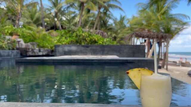 Refreshing cocktail in glass on stone surface near swimming pool at tropical resort. Camera moving up