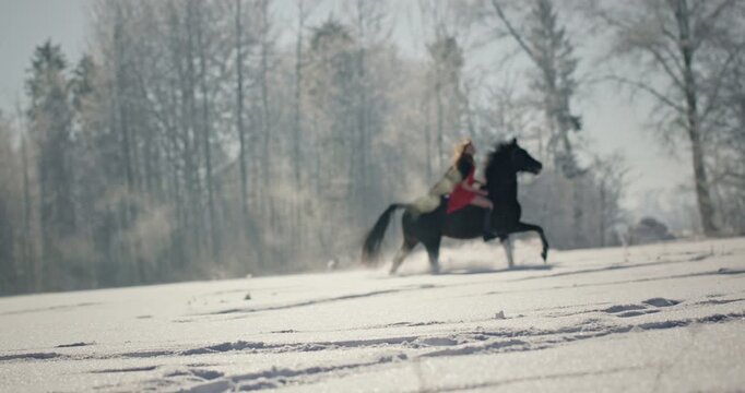 Woman riding a black horse gallopping in winter snow