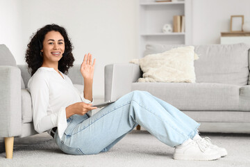 Fototapeta premium Female African-American online business consultant with laptop waving hand at home